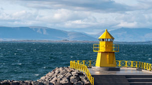 Yellow lighthouse tower on stone breakwater, entrance to Reykjavik port