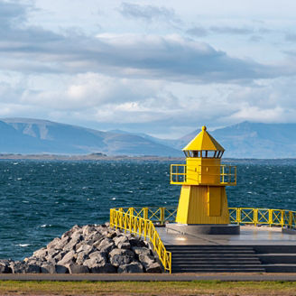 Yellow lighthouse tower on stone breakwater, entrance to Reykjavik port