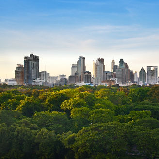 Bangkok skyline with modern high-rise buildings behind a large green park under a clear blue sky
