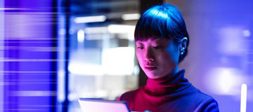 Person indoors holding and interacting with a tablet, with a blurred background and vibrant purple-blue lighting