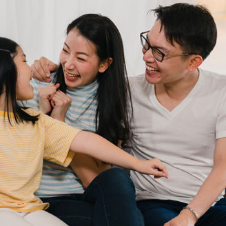 Happy Asian young family homeowners bought new house. Japanese Mom, Dad, and daughter embracing looking forward to future in new home after moving in relocation sitting on sofa with boxes together.