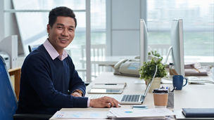 Portrait of smiling Vietnamese businessman sitting at workplace and looking at camera, Portrait of smiling Vietnamese businessman sitting at workplace and looking at camera