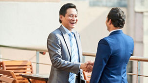 Asian mature businessman in suit greeting his business partner in outdoor cafe, he smiling and shaking his hand