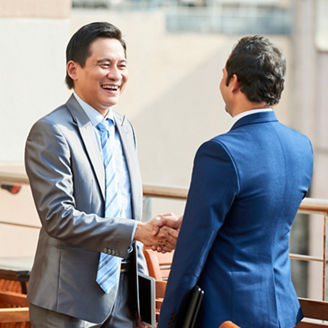 Asian mature businessman in suit greeting his business partner in outdoor cafe, he smiling and shaking his hand