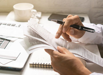 A business man holding pen while looking at the bills in his workplace. Business concept.