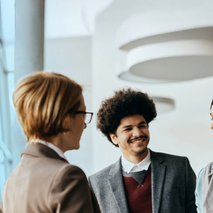 Three people talking next to a large glass window inside of a building