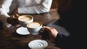 Close-up of a man and woman clinking a white coffee cup in a coffee shop representing domestic business in Budget 2027