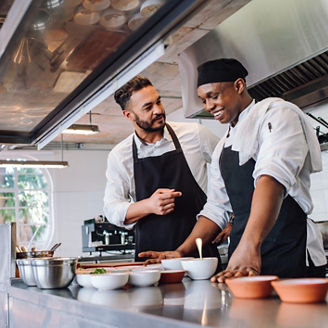 Happy men chefs cooking food at cafe kitchen representing indirect taxes in Budget 2027