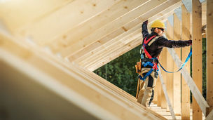 A worker stands on a wooden roof frame at a construction site representing property and construction in Budget 2027