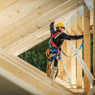 A worker stands on a wooden roof frame at a construction site representing property and construction in Budget 2027