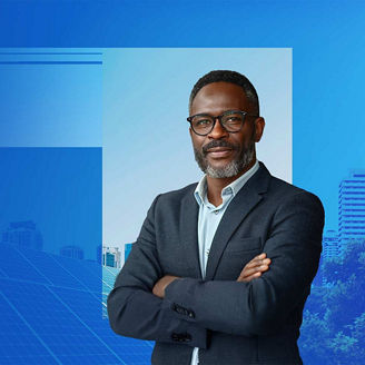 CEO looking into camera with solar panels and wind turbines behind