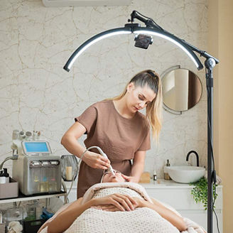 Professional esthetician using hydrafacial equipment on female client during beauty procedure in modern skincare studio