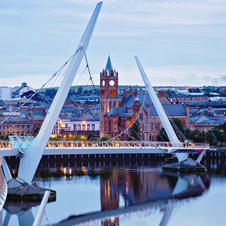 Derry, Ireland. Illuminated Peace bridge in Derry Londonderry, City of Culture, in Northern Ireland with city center at the background. Night cloudy sky with reflection in the river at the dusk