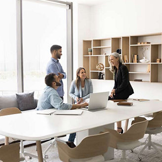 Small younger business group and elder leader woman talking at large table in modern contemporary office space