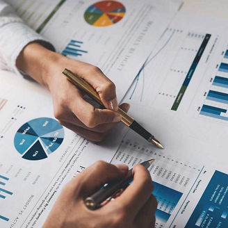 Hands pointing pens at charts representing financial services