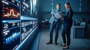 Project Manager and Computer Science Engineer Talk while Using Big Screen Display and a Laptop