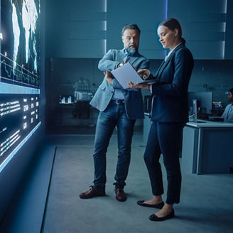 Project Manager and Computer Science Engineer Talk while Using Big Screen Display and a Laptop
