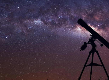 Telescope on tripod in field under starry sky