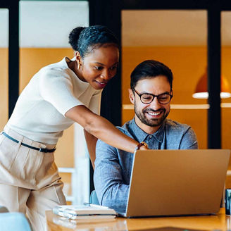Two young professionals, a man and a woman, share ideas while reviewing work on a laptop in a corporate office setting, representing from start-up to scale-up