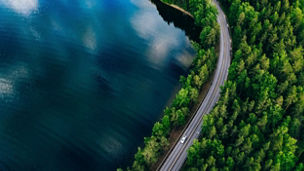 Aerial view of road between green summer forest and blue lake in Finland