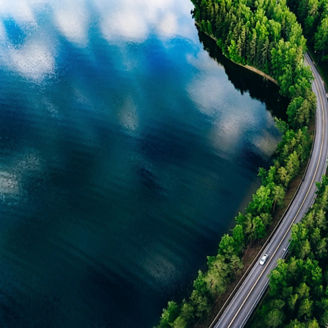 Aerial view of road between green summer forest and blue lake in Finland
