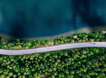Aerial view of road between green summer forest and blue lake in Finland