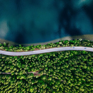 Aerial view of road between green summer forest and blue lake in Finland