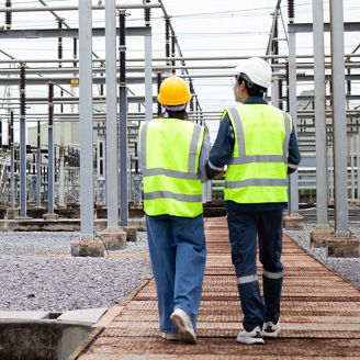 Engineer is working at high voltage substation wearing safety gear and reflective vest while inspecting electrical equipment in industrial outdoor environment
