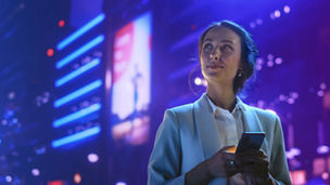 Woman with smartphone looks up at the city lights