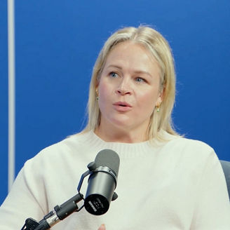 Person speaking into a microphone in a podcast recording studio with a blue background