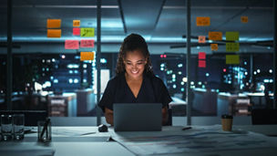 Portrait of African American Businesswoman Working on Laptop Computer in Big City Office Late in the Evening. Female Executive Director Managing Digital e-Commerce Project, Finance Analysis
