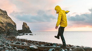 Man hanging in the balance over a log at seaside in Scotland - Hiker having fun at beautiful destination Talisker bay after the rain - Filter applied, travel and adventure concepts