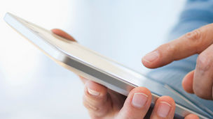 Hand holding digital tablet over stack of books
