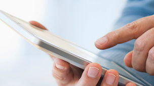 Hand holding digital tablet over stack of books