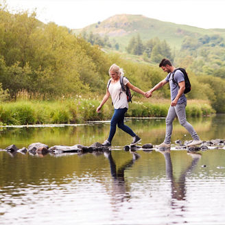 man-woman-stepping-stones-lake-mountain