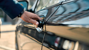 Cropped photo of a male hand opening the door of a black car while standing outdoors. Close up. Transportation