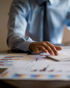Businessman using a calculator on a table with printed graphs and reports
