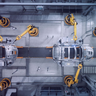 Overhead view of an automotive assembly line with multiple yellow robotic arms working on car bodies positioned along a central conveyor