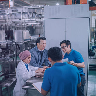 Workers gathered around a workstation discussing documents inside a beverage production facility