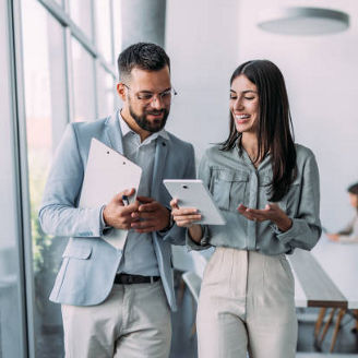 Shot of a two confident business persons talking in the work place. Two colleagues using a digital tablet while walking in a modern office. Businessman and businesswoman in meeting discussing business strategy. Business coworkers working together in the offic