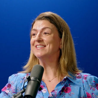 Person speaking into a microphone in a studio setting against a blue background with vertical light accents