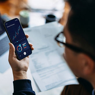 Young Asian man managing finance and investment online, analyzing stock market trades with smartphone and laptop. Making financial plans. Banking and finance, investment, financial trading, mobile banking with technology concept