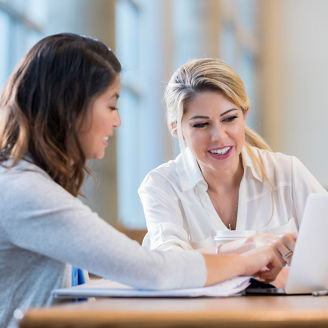Diverse female college students review something on a laptop while studying for an exam.