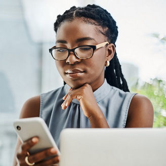 Young black businesswoman using a cellphone while working on a laptop in an office alone