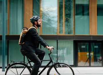 Side view of a city commuter riding to work on a bicycle. Young single businessman traveling from work to home on a bike, wearing a backpack and helmet for safety. Full length shot with copy space. City lifestyle of single man.