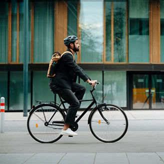 Side view of a city commuter riding to work on a bicycle. Young single businessman traveling from work to home on a bike, wearing a backpack and helmet for safety. Full length shot with copy space. City lifestyle of single man.