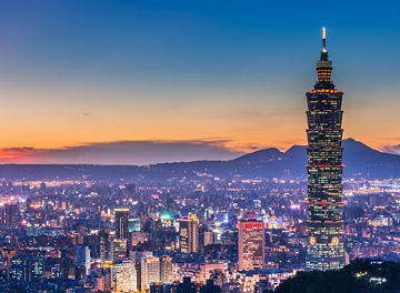 High angle shot of Taipei 101 at night with sunset afterglow in the back and city lights.