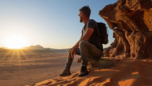 Male tourist sitting on rock ledge watching desert sunset, Wadi Rum, Jordan; Shutterstock ID 2707188247; purchase_order: MKTG-OM; job: ; client: ; other: 