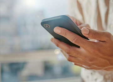 窓辺に立ちスマートフォンで情報を確認する一人の男性