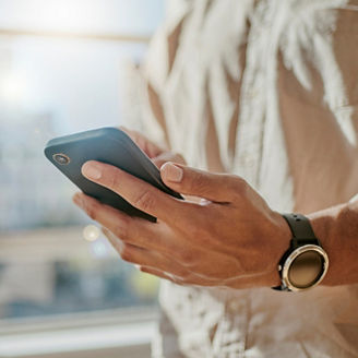 窓辺に立ちスマートフォンで情報を確認する一人の男性